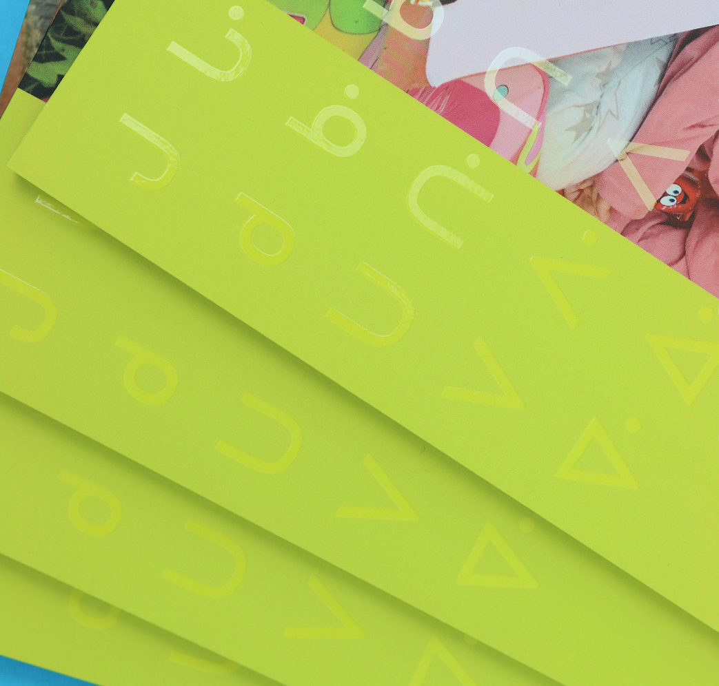 CSB_202223_Body-2 Bright yellow-green cards with glossy, abstract symbols and shapes overlap on top of colorful, partially visible magazine pages featuring bold, playful images.