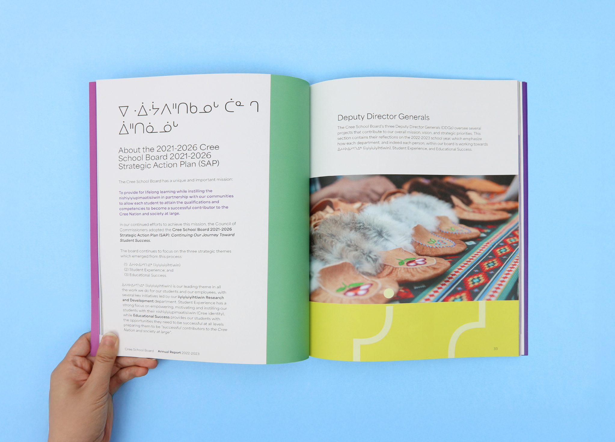 CSB_202223_Body-7 An open magazine showing text about the 2021–2026 Cree School Board Strategic Action Plan on the left page, and a photo of beaded moccasins and fur on a colorful fabric on the right page. A hand holds the magazine.