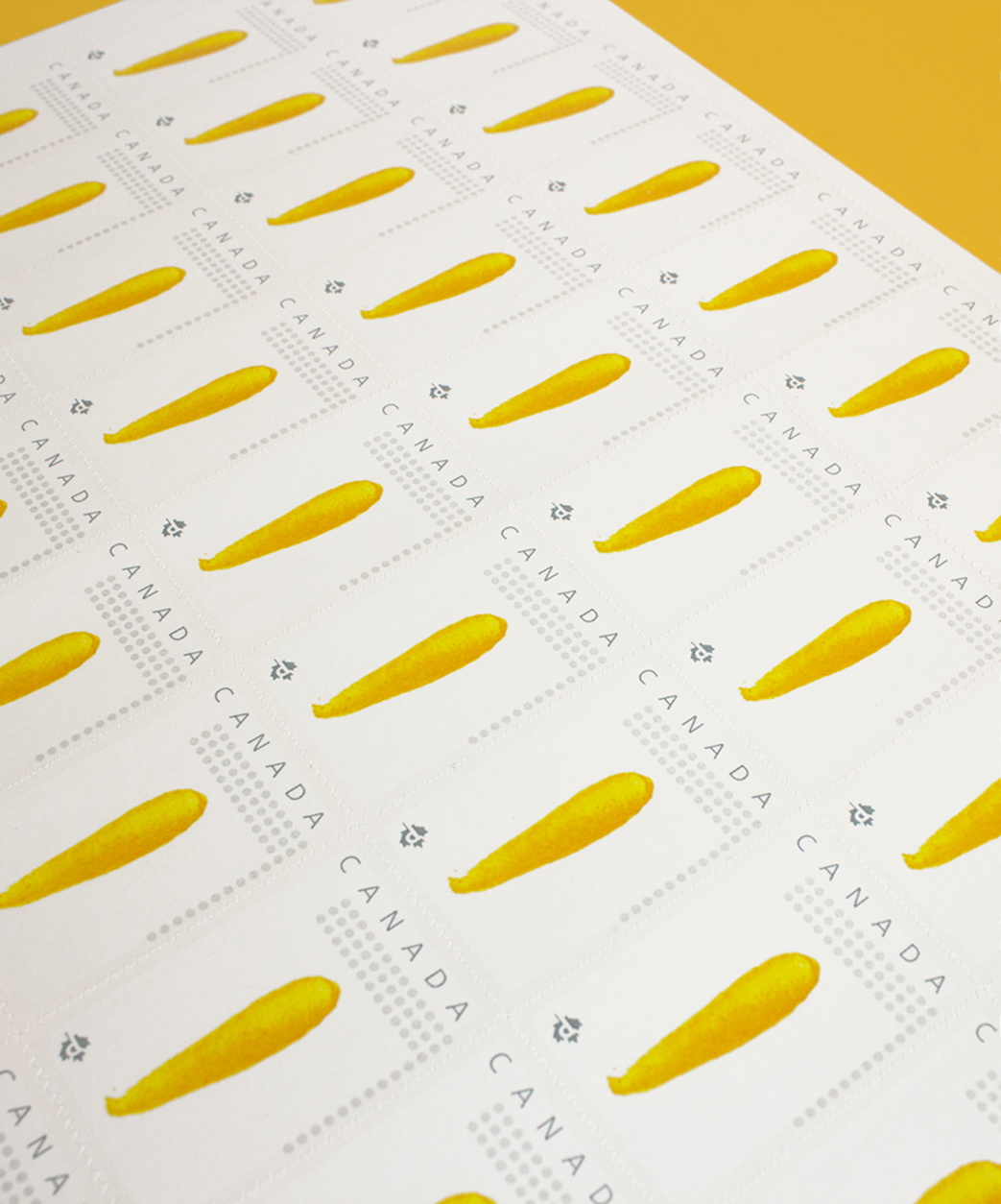 DontGetitTwisted_HolidayCard_2 A sheet of Canadian postage stamps featuring a simple illustration of a single yellow carrot on each stamp, arranged in neat rows on a white background.