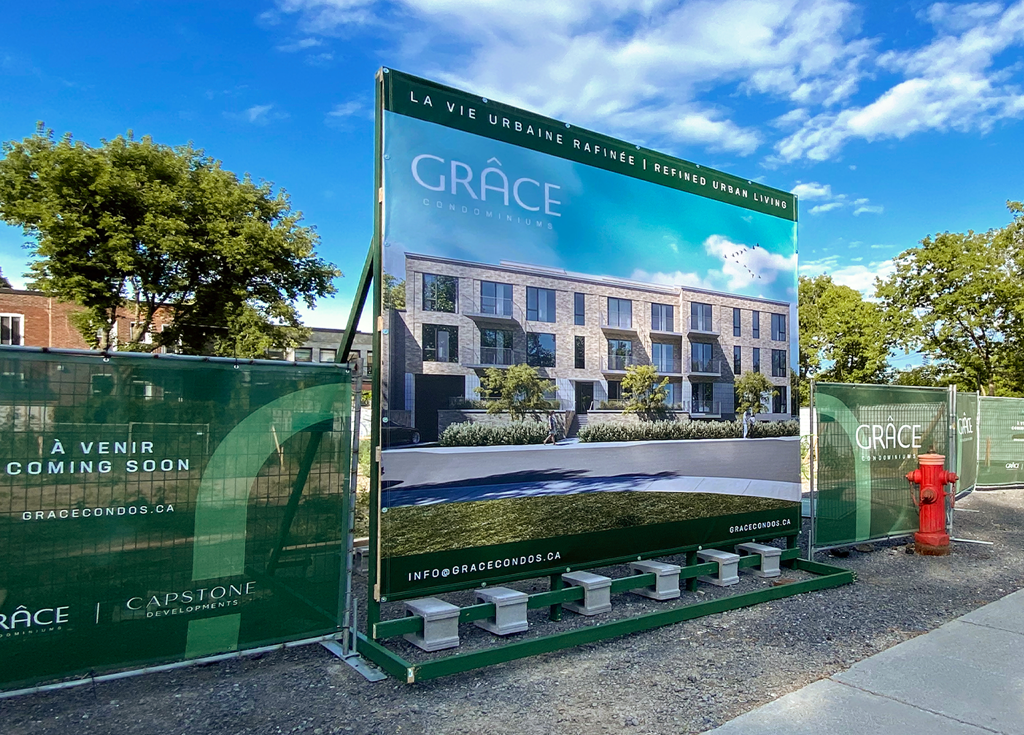 Grace_1 A large billboard displays a modern condo building rendering at a construction site, surrounded by green fencing with