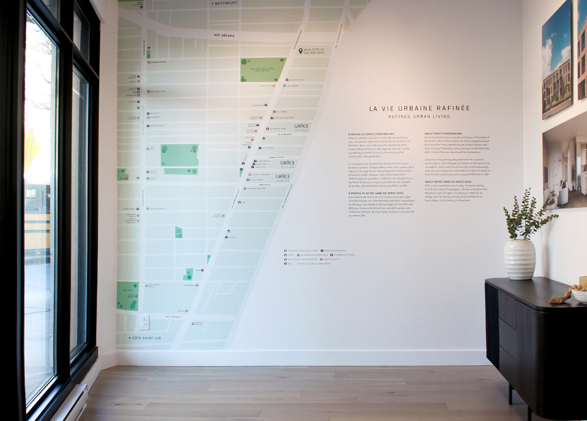 Grace_6 A modern, bright room with a large map and descriptive text on the wall, a window on the left, and a black console table with a vase of greenery on the right.