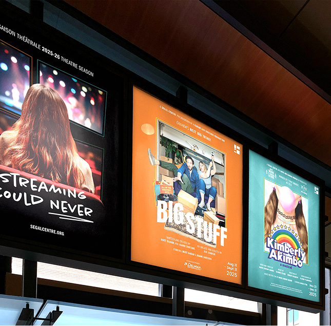 Three theater posters displayed side by side indoors; the left poster shows a person with long hair from behind, the middle depicts three people sitting with moving boxes, and the right features stylized text with more long hair artwork.