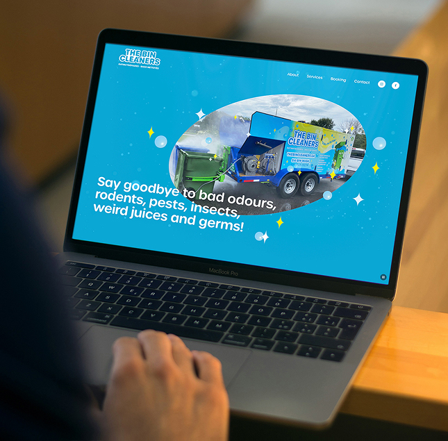 A person uses a laptop displaying The Bin Cleaners website, which shows a trailer with cleaning equipment and the text:
