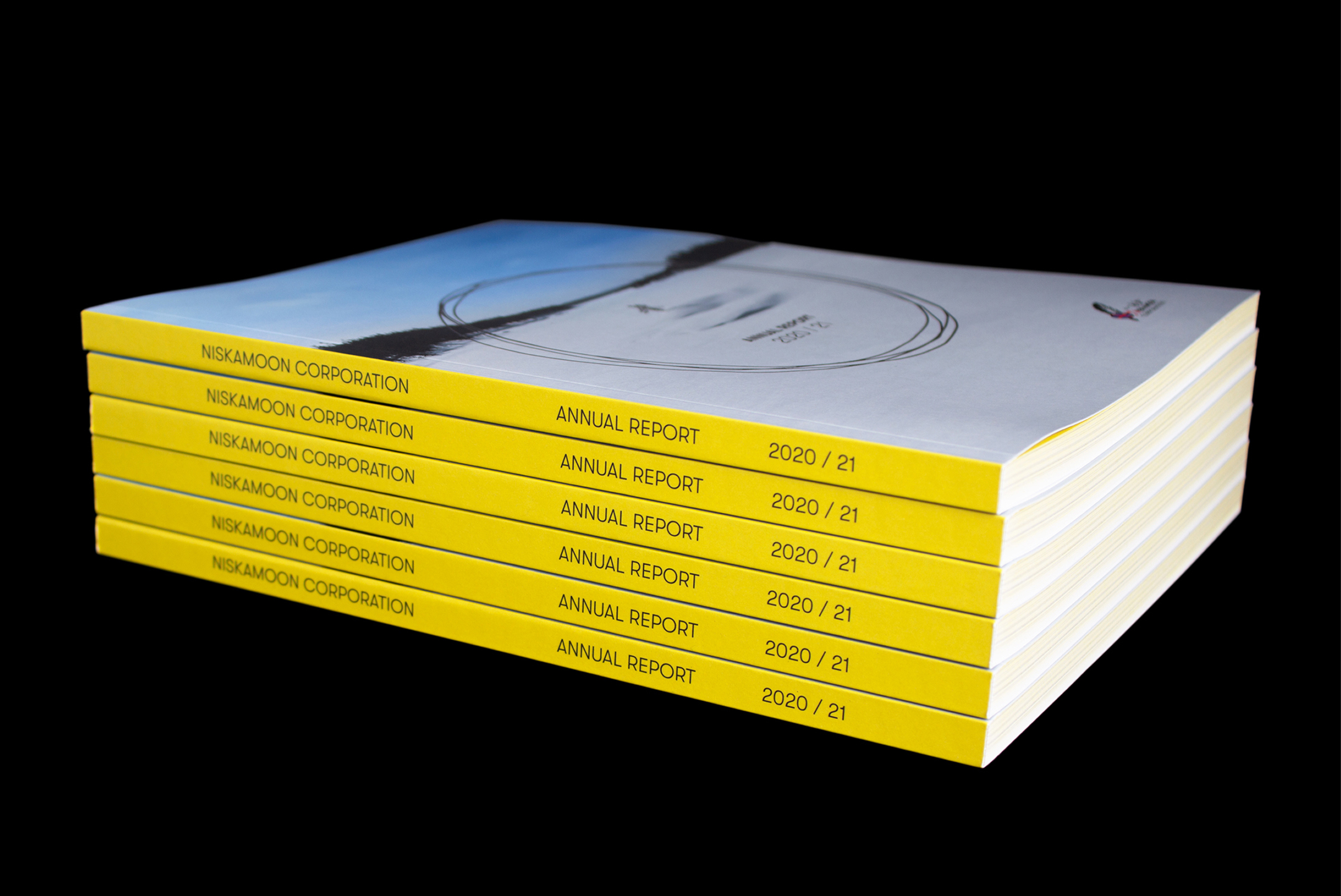 A stack of six annual reports with yellow spines labeled "Nisga’a Nation Corporation Annual Report 2020/21" sits against a black background. The cover features a circular design with blue and white colors.