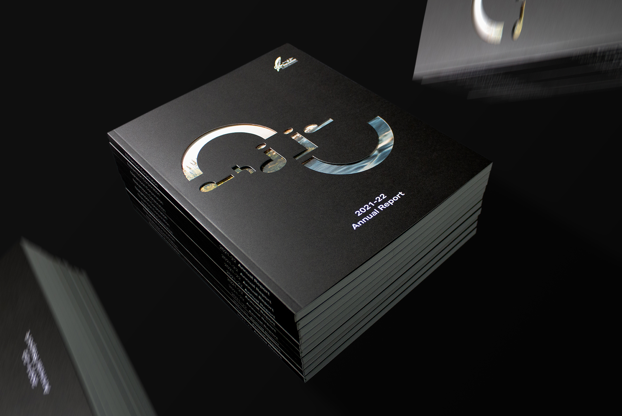 A stack of annual reports with a black cover that features a large cut-out design and text reading "2021–22 Annual Report" on the front, placed on a dark surface.