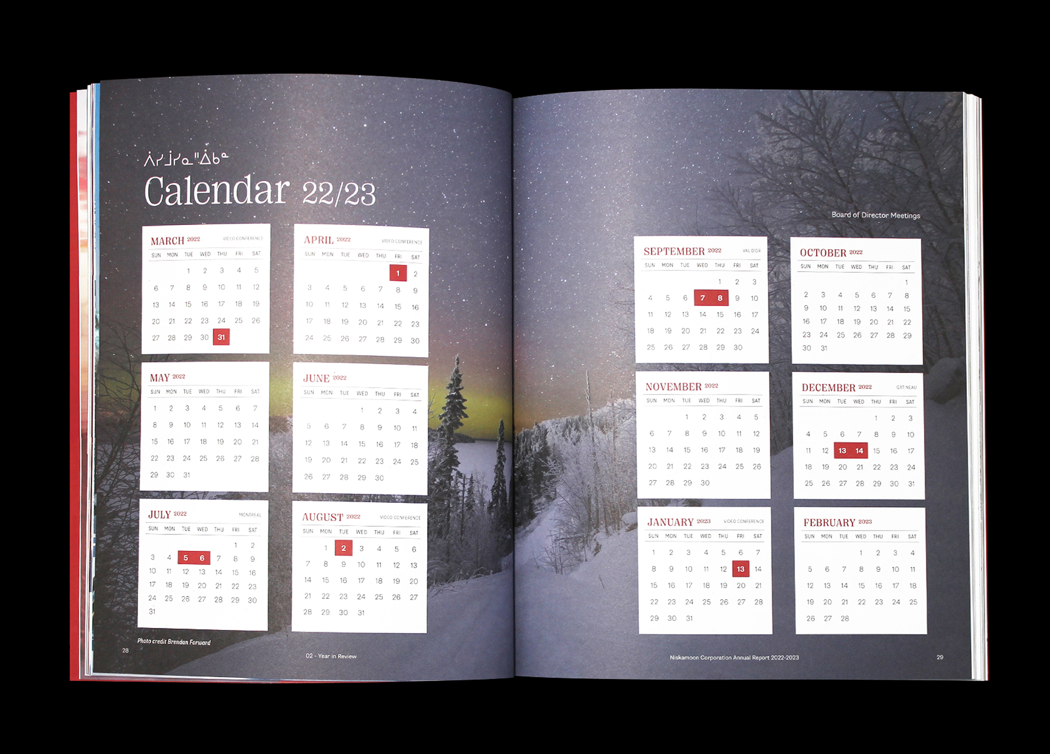 Niskamoon_202223-6 An open book displays a 2022/2023 calendar with months arranged in a grid over a snowy, tree-lined landscape at dusk; red squares highlight specific dates. Text appears in both English and another language.