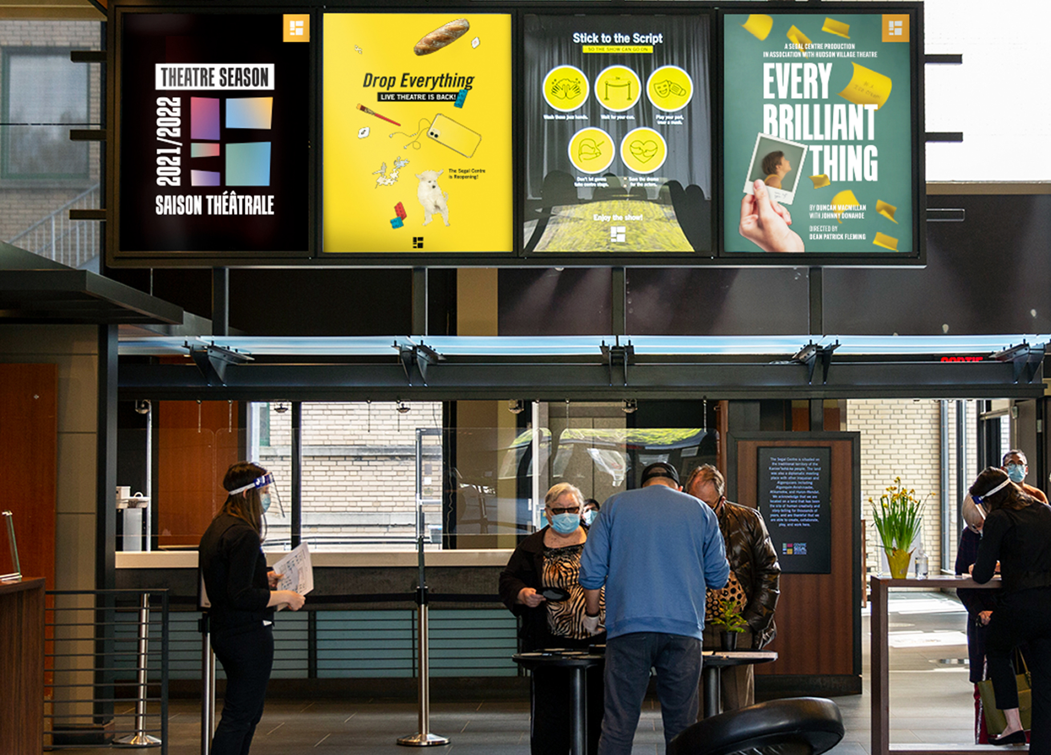 Segal_202122-1 People check in at a theater lobby with staff at a counter. Four colorful posters for various theater productions are displayed above, promoting the current theater season. Some staff wear face shields or masks.