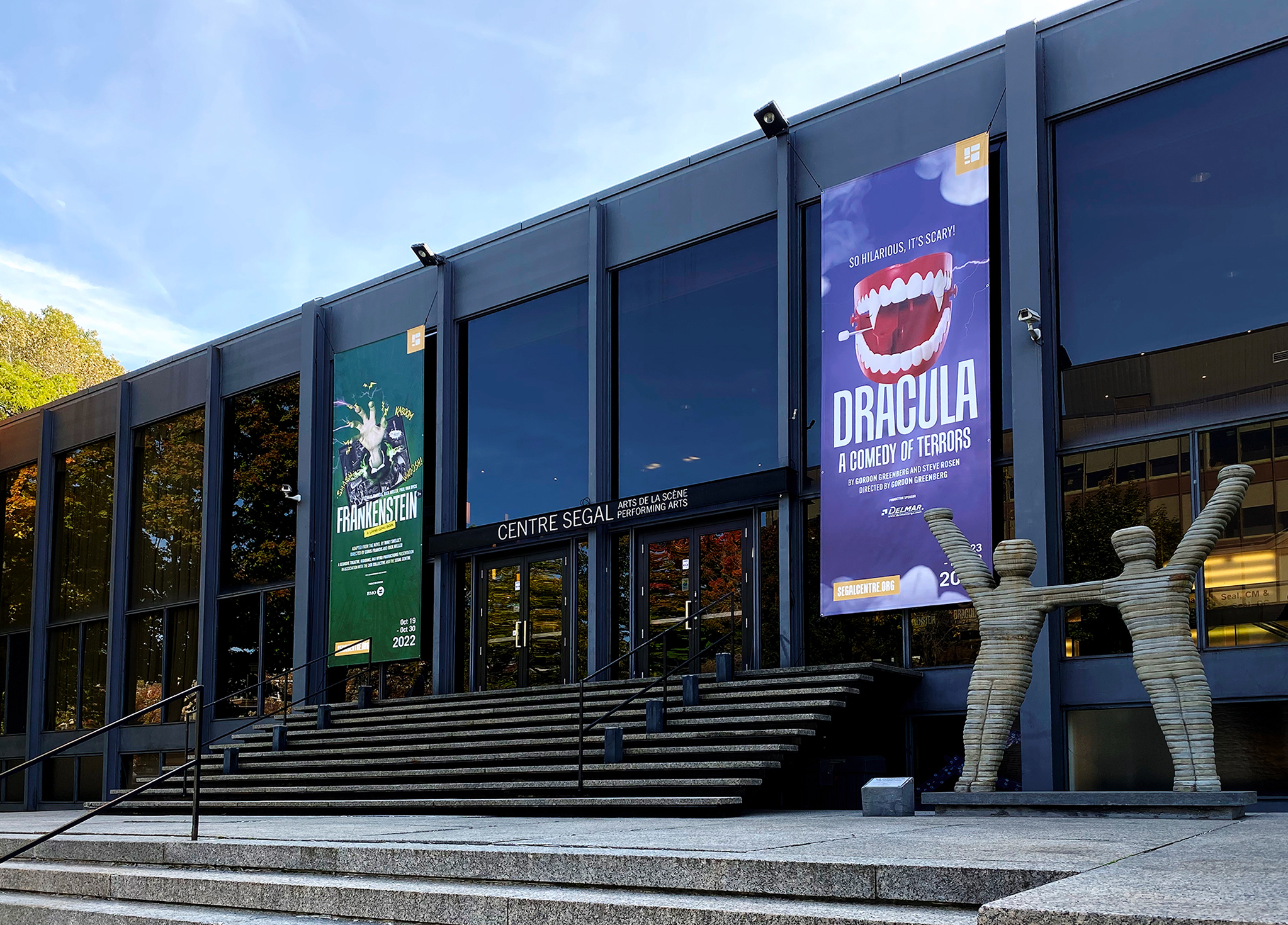 Segal_202223-3 Modern building entrance with wide stairs, large glass windows, and two banners advertising