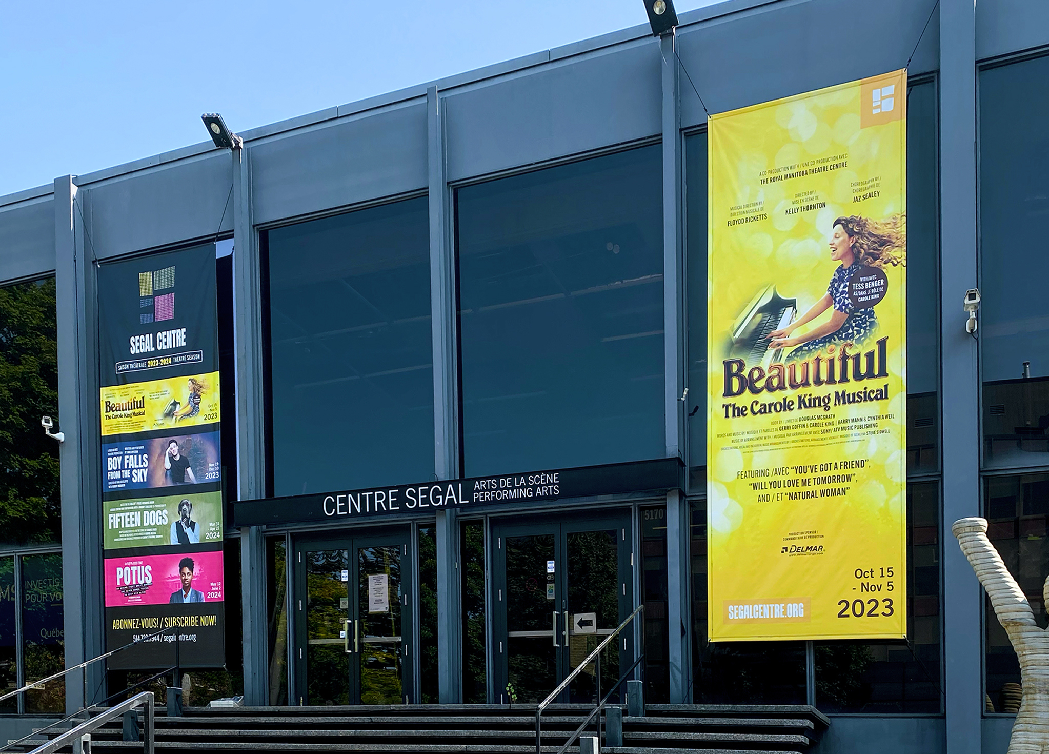 Segal_202324-1 The exterior of Centre Segal, a performing arts building with large glass doors. Colorful posters for various theater productions, including
