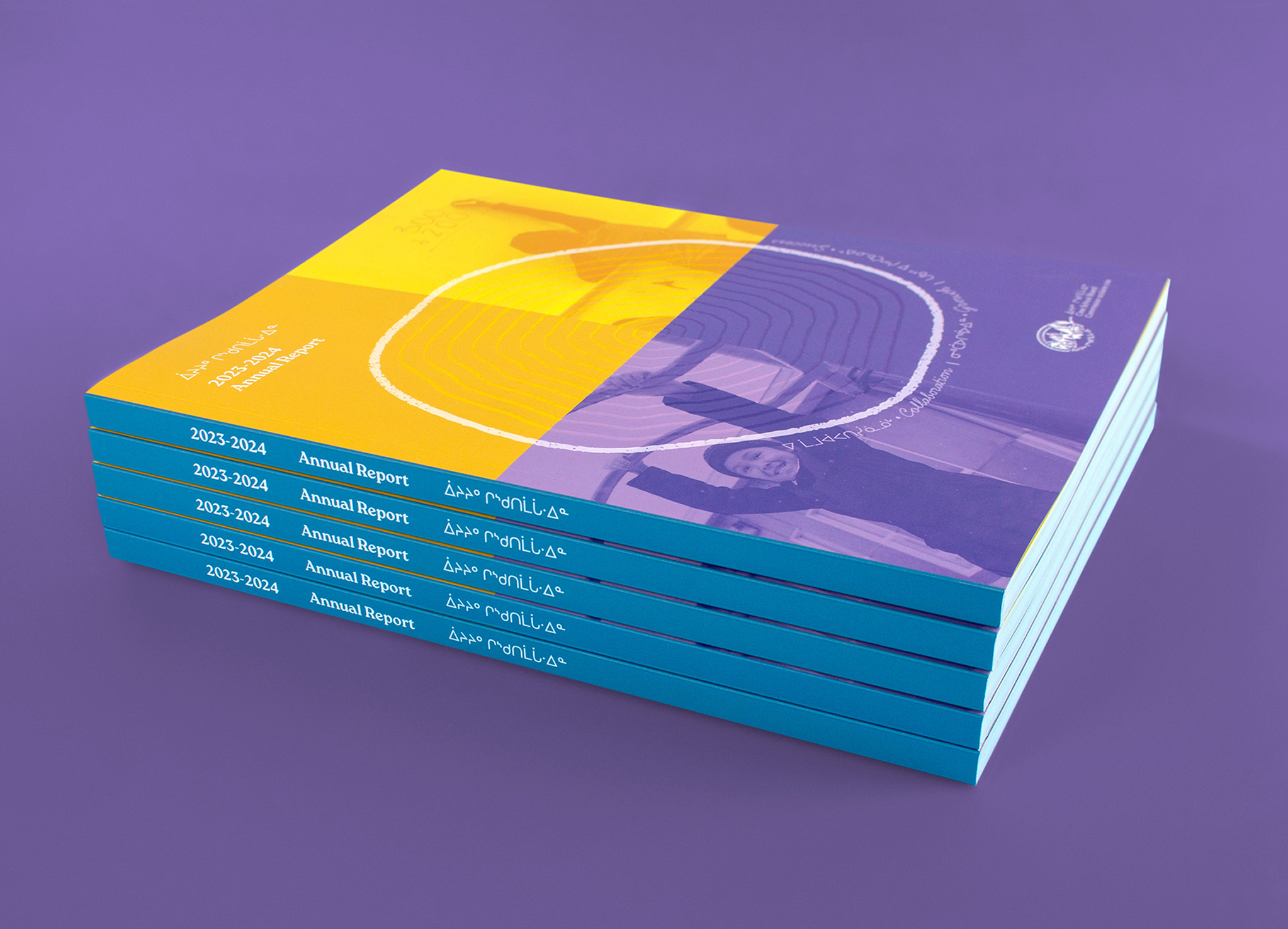 CSB_202324-1 A stack of colorful annual report booklets for 2023–2024 with teal spines, lying on a purple surface. The covers feature abstract designs in yellow and blue with white circular patterns and partial images of people.