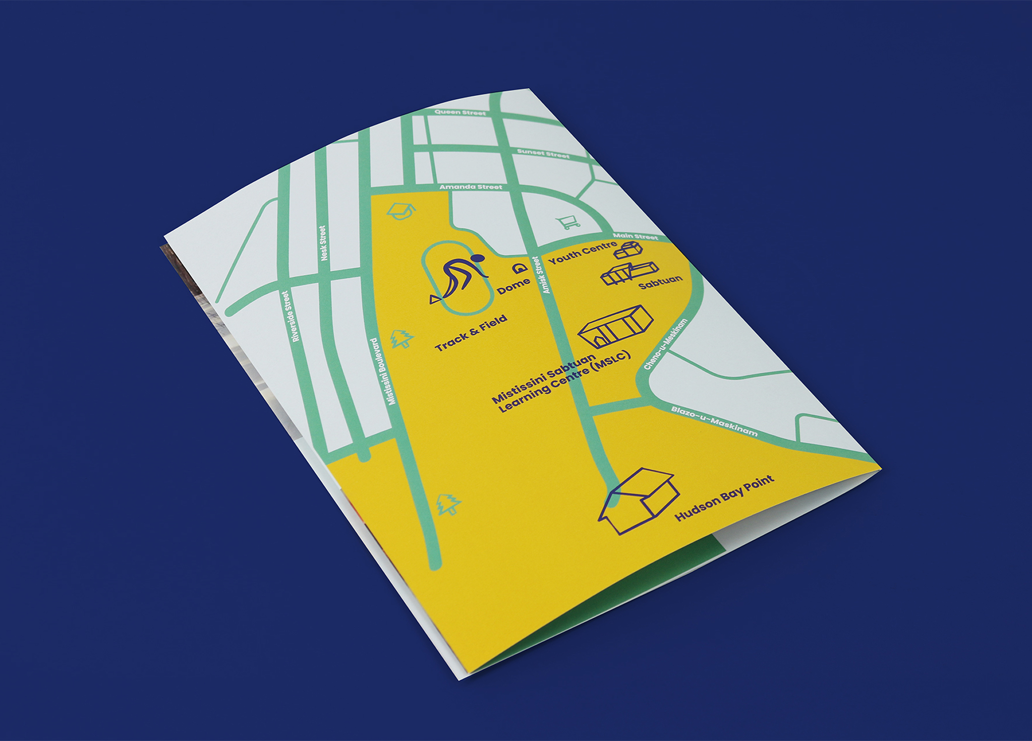 A folded map on a blue surface shows simplified green streets, yellow areas, icons for major spots like a stadium, visitors center, landmark sculpture, and Hudson's Bay Point, plus labeled paths and symbols.