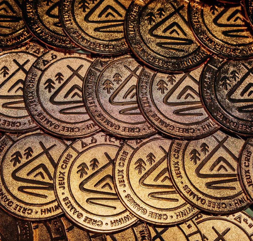 A close-up view of numerous bronze-colored game tokens with embossed logos, trees, and text reading