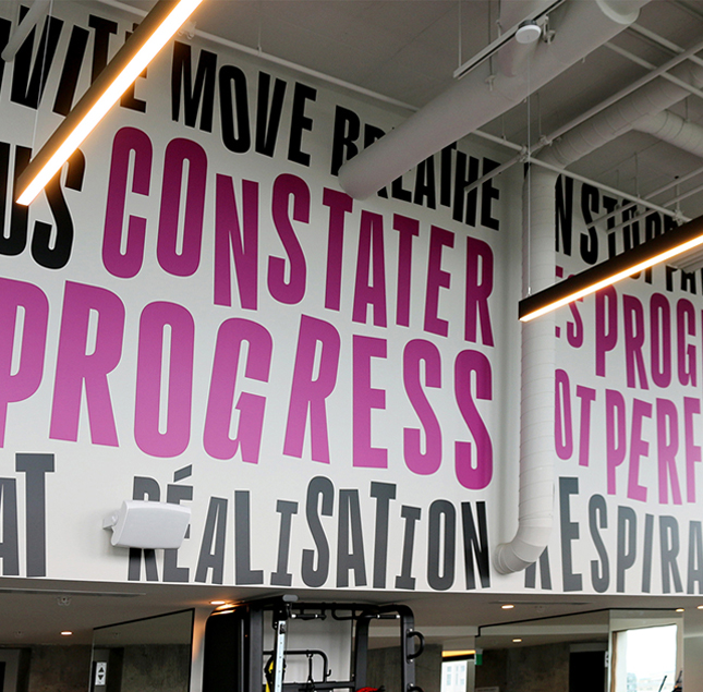 A modern interior wall features large, bold text in black and magenta, with the French words