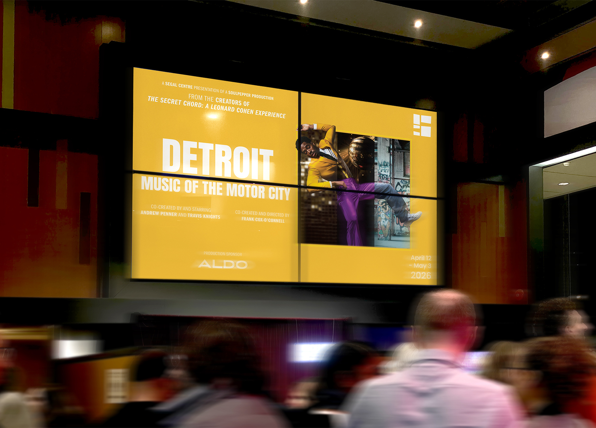 A large digital display in a modern venue shows a yellow poster for